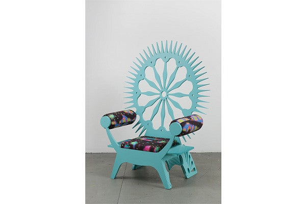 Michael Rey chair. Teal painted/colored wood with a busy stuffed pattern on the arms and seat of the chair. Chair has a circular starburst design on the back. 