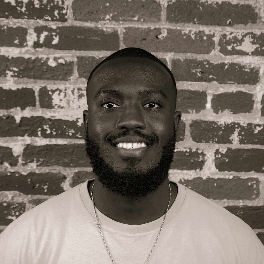 Photograph of a smiling first-year SPD student, Maxwell Prempeh, in front of a brick wall.