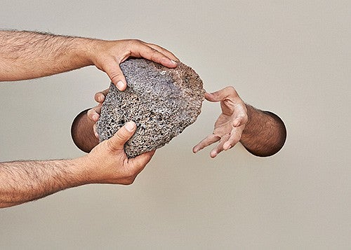 photo of hands passing rock
