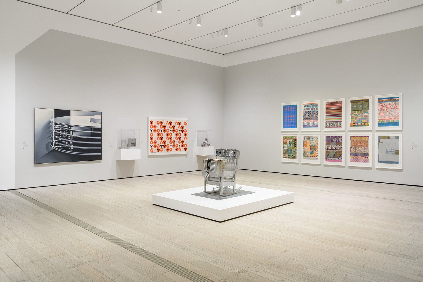 Room full of vibrant art pieces. A sculpture of a rusted metallic silver rocking chair stands in the middle.