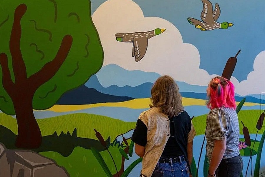 Photograph shows two students looking at an artistic mural of two ducks