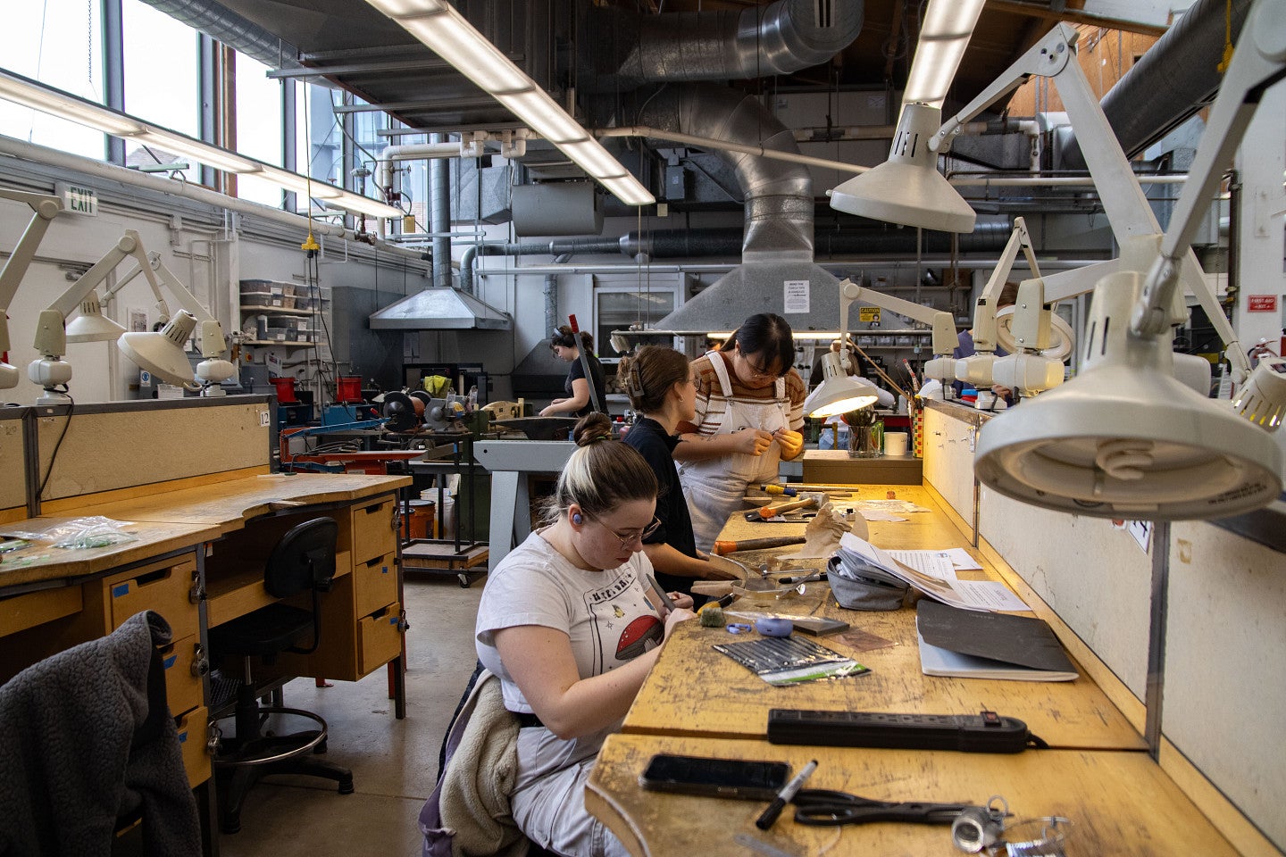 Students talk with faculty member in jewelry and metalsmithing studio. Decorative. 