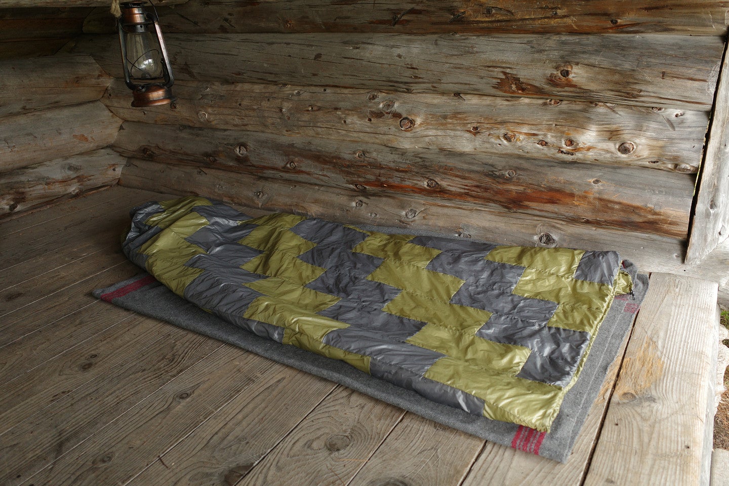 Shows a hand-made quilt in a log cabin-esque room. 