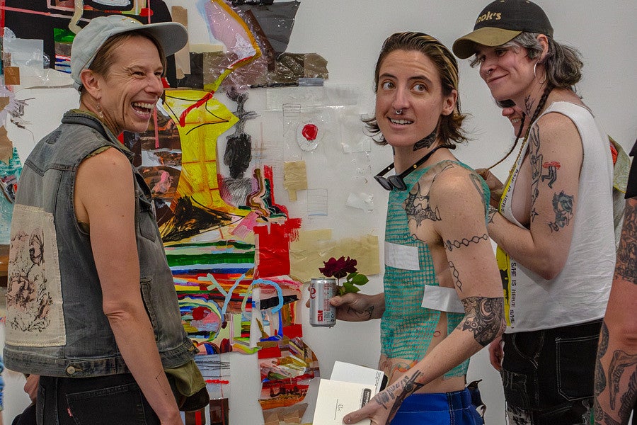 Elri looks off to the side with friends at their MFA exhibition at Ditch Projects. 
