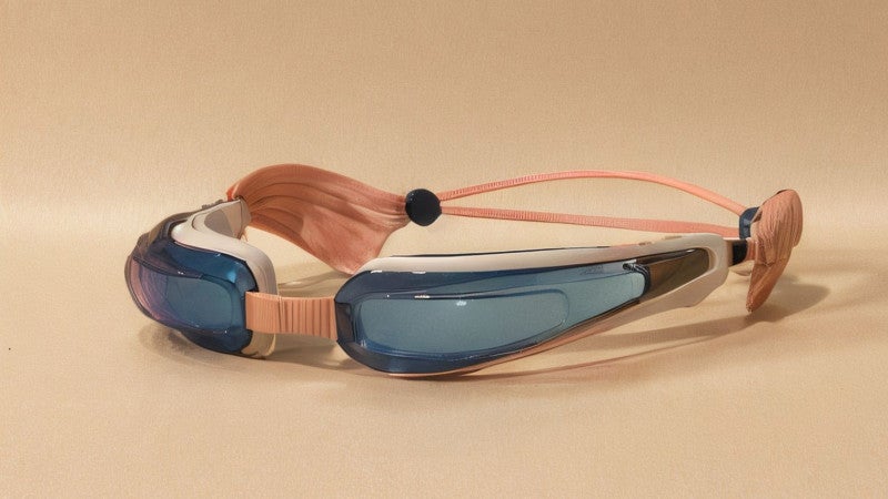 A pair of very thin goggle with blue lenses, white rubber seals, and an earthy pink strap.