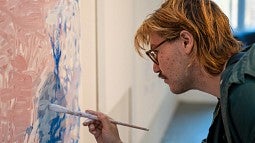 News Header for MFA Story. Shows a close up of a painter in the middle of painting. 