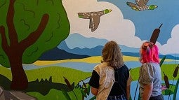 Photograph shows two students looking at an artistic mural of two ducks 