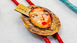 Jewelry Sale news header, shows a close up of a necklace with a vintage women's face surrounded by a round, metal frame that is reminiscent of reptile skin and corded with a red cord. 