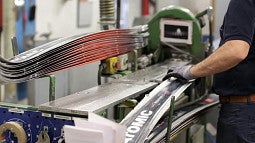 Shows a worker next to a machine that is making skis. 
