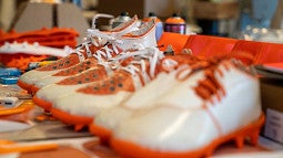 Orange prototype cleats are arranged in a line on a desk. 