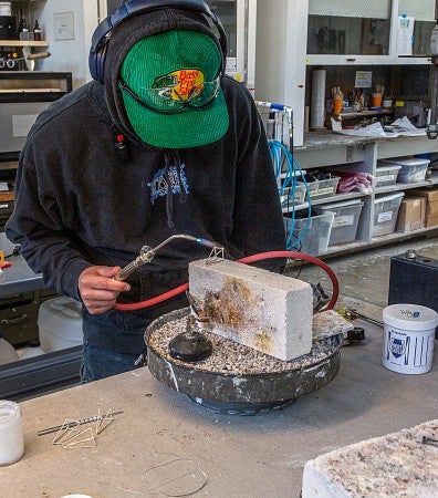 Photograph of a student working on jewelry with a torch. 