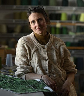 Headshot of Kate Nartker. Shows a woman in front of different looms, smiling. 