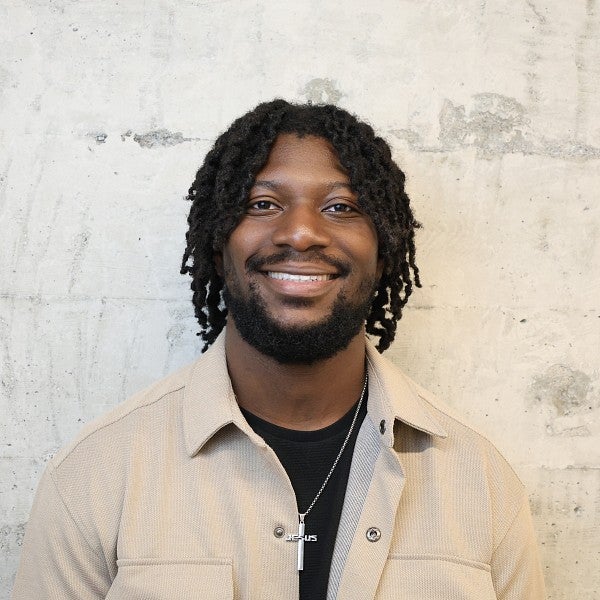 Photograph of Toluwalase Adedipe. Shows a smiling, bearded individual with medium length locs