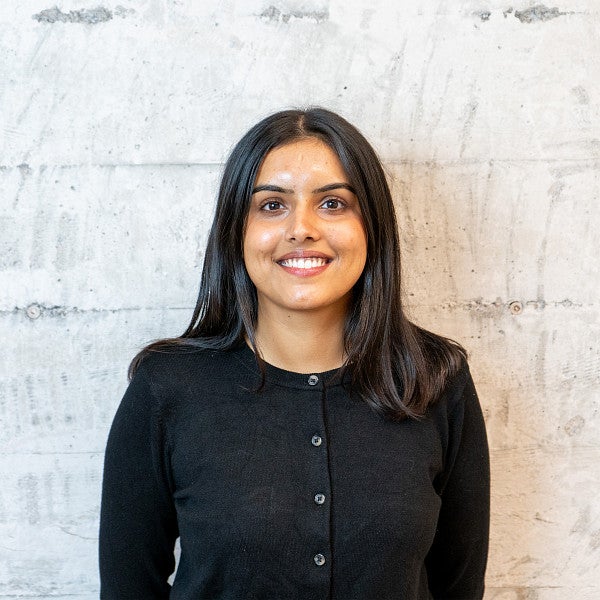 Femme presenting individual with long, dark hair smiles into the camera in front of a wall.