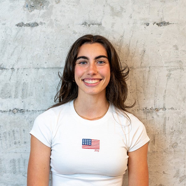 Femme presenting individual smiles into the camera in front of a concrete wall. 