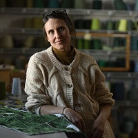 Headshot of Kate Nartker. Shows a woman in front of different looms, smiling. 